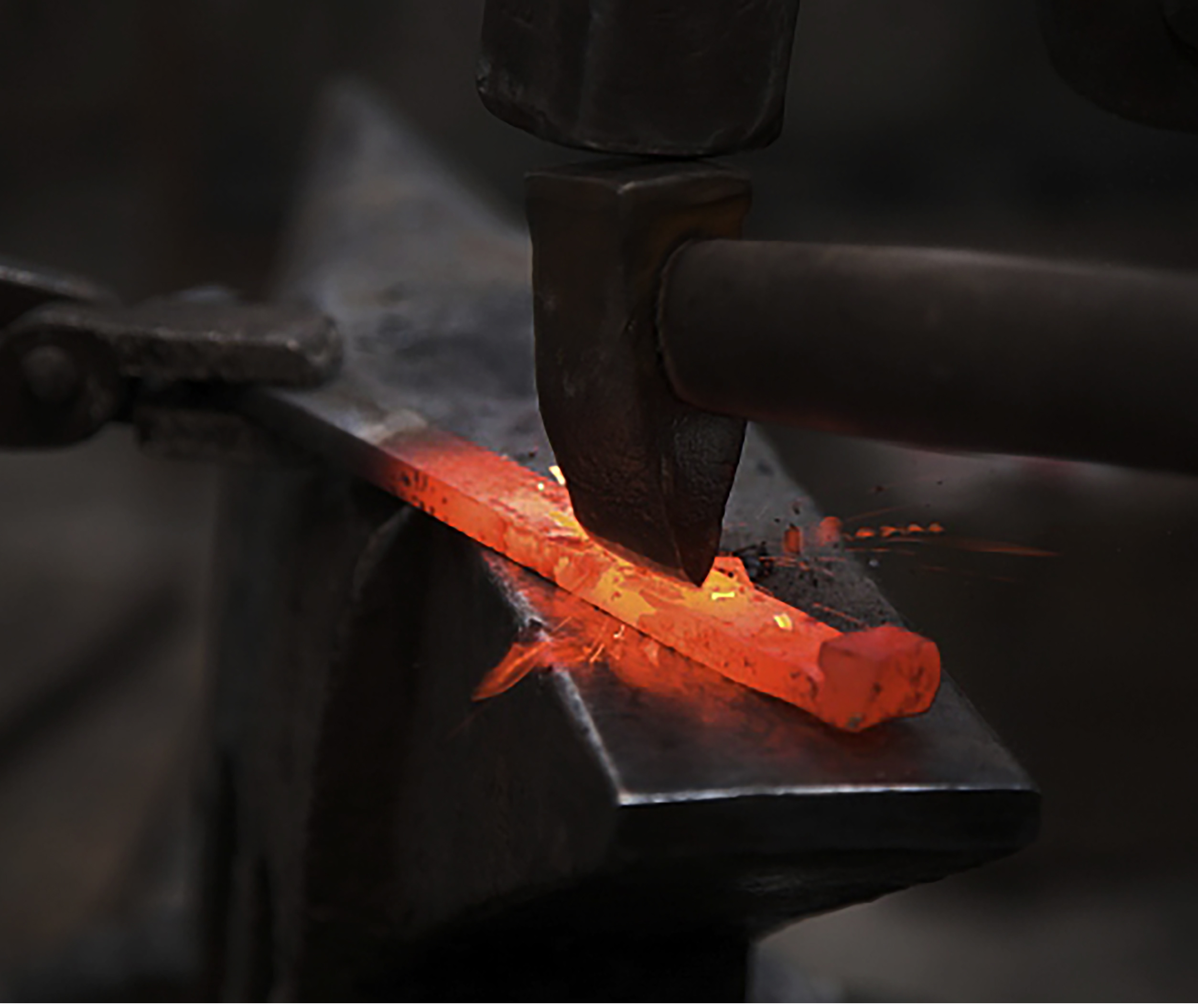 鍛冶職人が熱い金属を叩いている写真